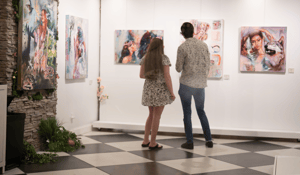 Man and Woman standing in white gallery bold color painitngs on the wall